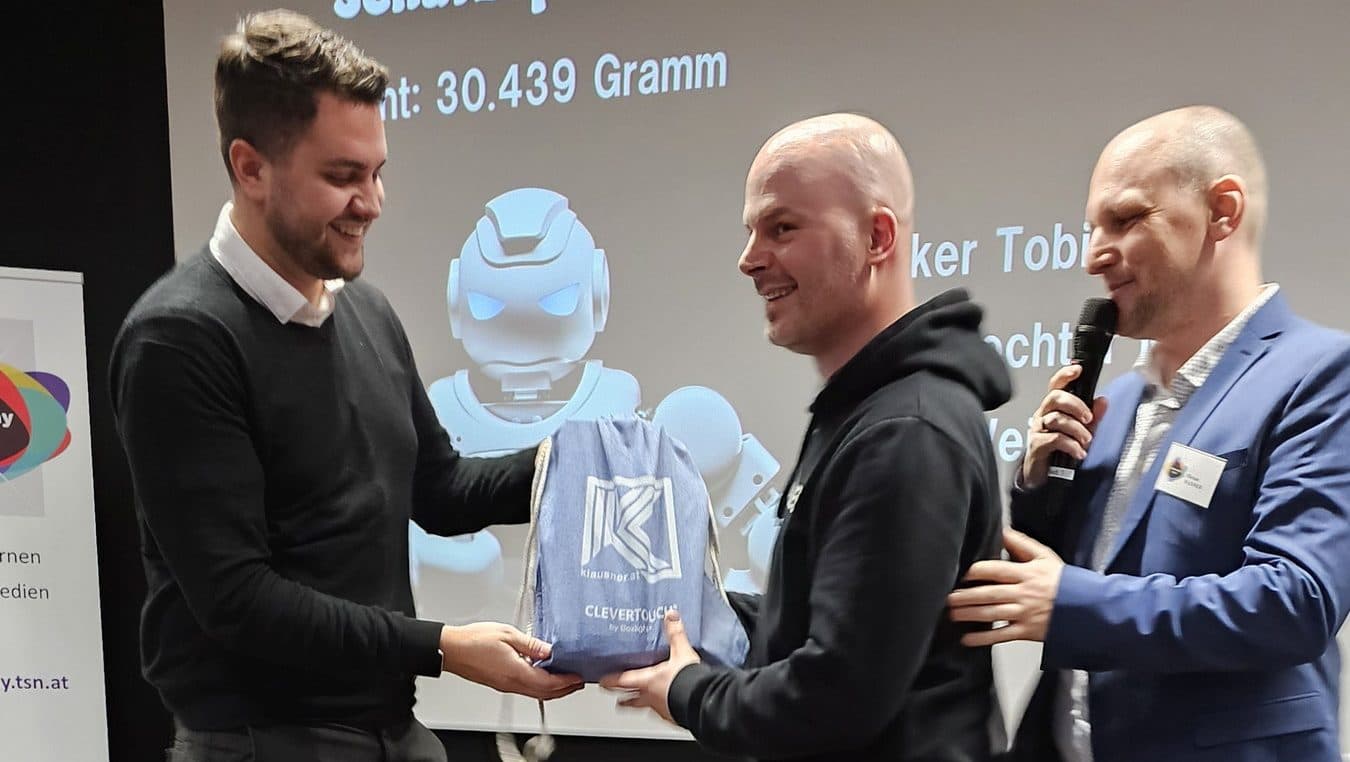 Luca Albertini übergibt einen Preis, eine HoverCam Solo 8 Plus, an den glücklichen Gewinner während des eFuture Days an der PHT. Auf dem Hintergrundbildschirm sind Details zum Gewinnspiel sichtbar.