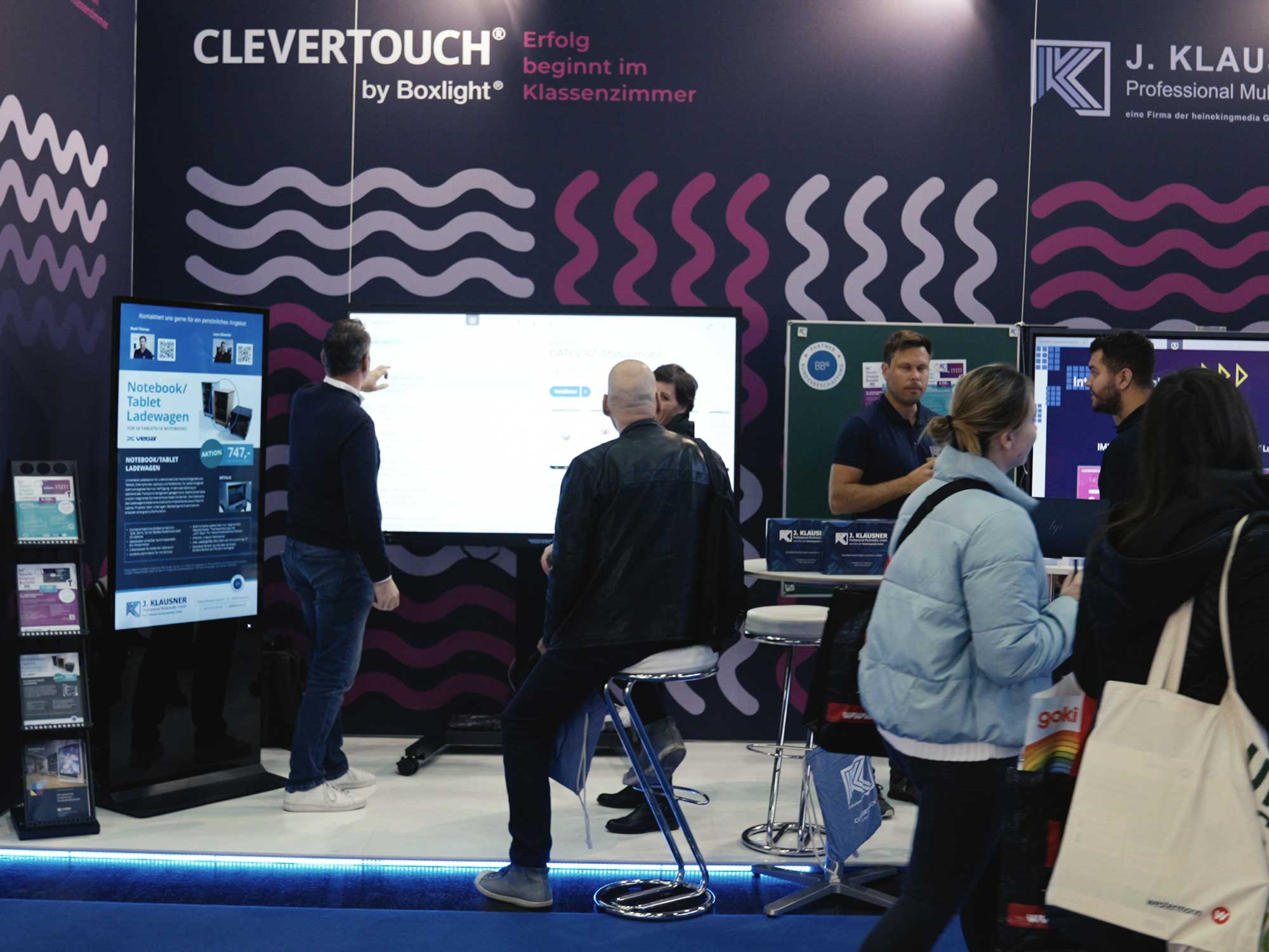 Besucher auf dem Klausner-Messestand der Interpädagogica 2024, mit interaktiven Displays, Informationsmaterialien und Gesprächen vor Ort.